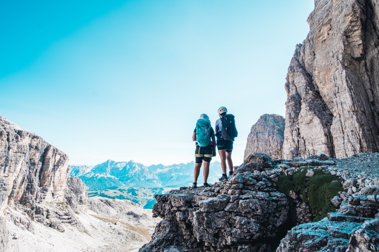 Zwei Menschen auf einem Felsen mit Blick auf die Berge an einem sonnigen Tag – symbolisiert Kommunikation auf Augenhöhe.